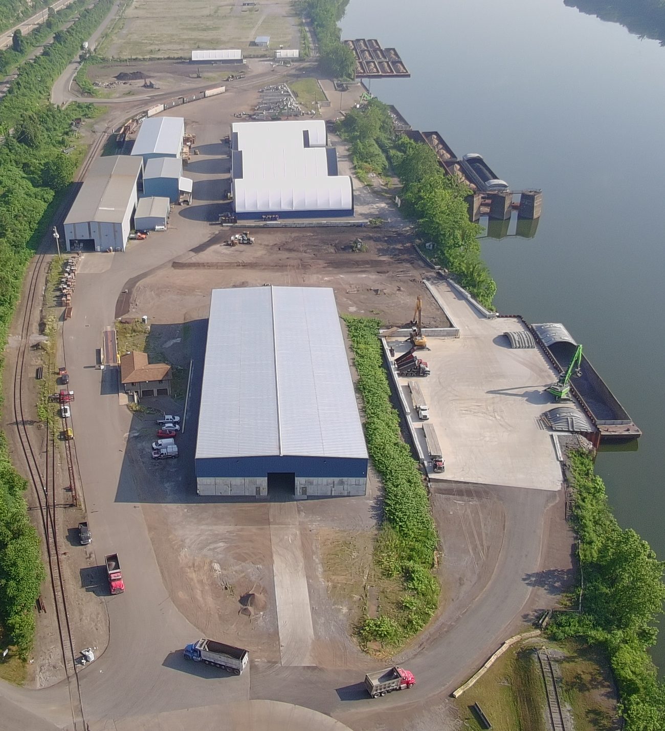 Aerial view of the terminal with warehouse buildings, laydown areas, and a crane and barges at the dock on the Ohio River.