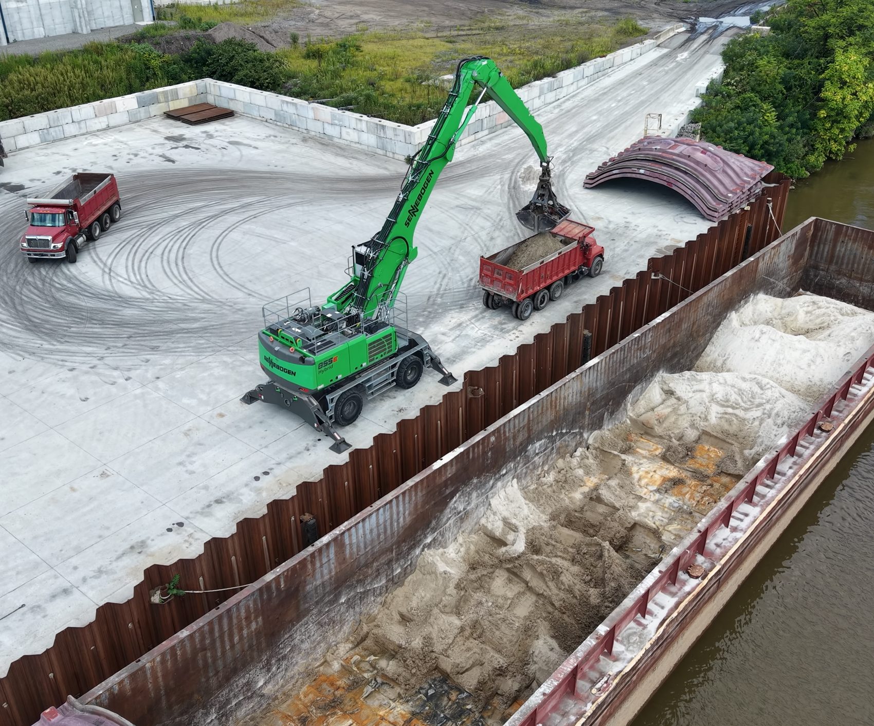 Material handler loading a red dump truck at the terminal, with a loaded barge on the Ohio River alongside.