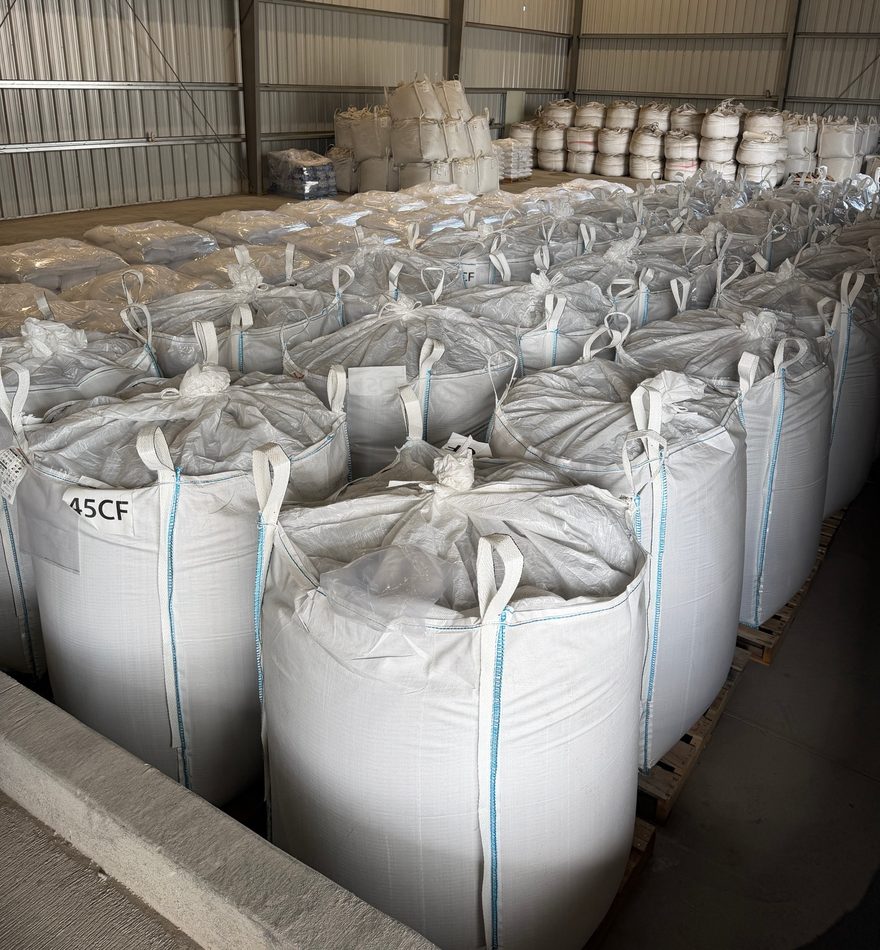 Rows of white super sacks in warehouse storage, with a lot number stenciled on the nearest bag.